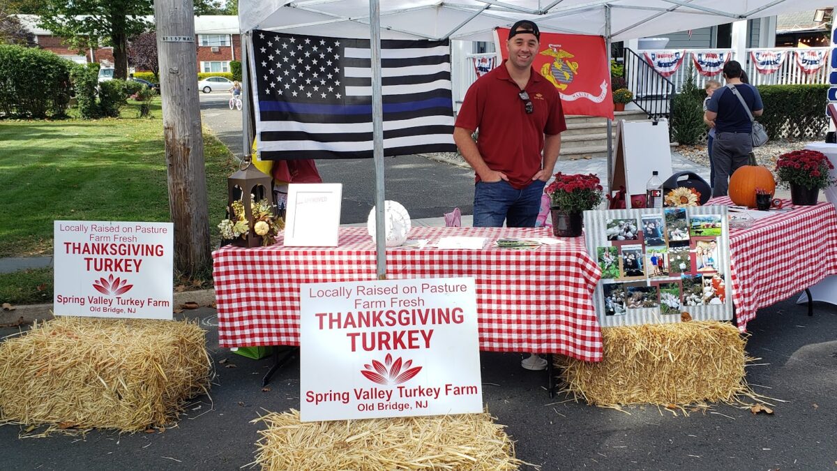 Spring Valley Turkey Farm booth at a local New Jersey event featuring farm-fresh Thanksgiving turkey signage, hay bales, patriotic flags, and display table.