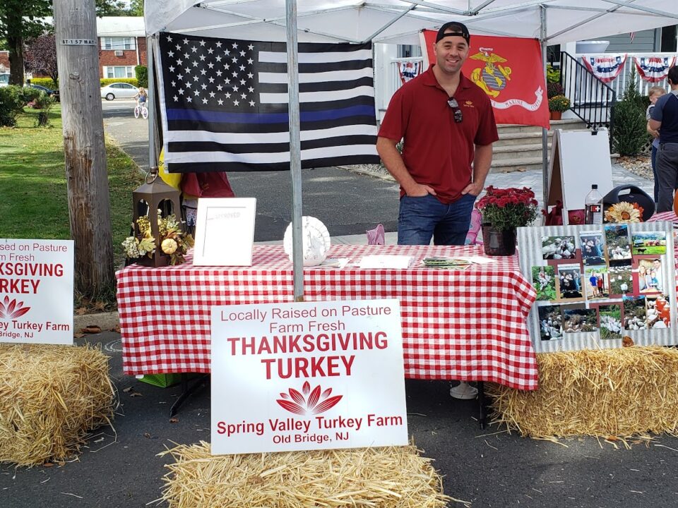Spring Valley Turkey Farm booth at a local New Jersey event featuring farm-fresh Thanksgiving turkey signage, hay bales, patriotic flags, and display table.