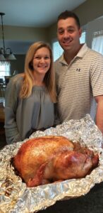 Smiling couple in a kitchen holding a freshly roasted turkey prepared for a family meal
