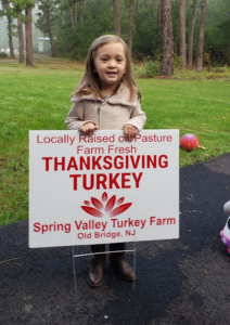 Young child holding a Spring Valley Turkey Farm sign promoting locally raised, pasture-raised Thanksgiving turkeys in Old Bridge, New Jersey.