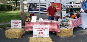 Veteran-owned Spring Valley Turkey Farm display booth at a local community event featuring Thanksgiving turkey signage, hay bales, farm photos, patriotic decorations, and information about locally raised pasture-raised turkeys in Old Bridge, New Jersey.